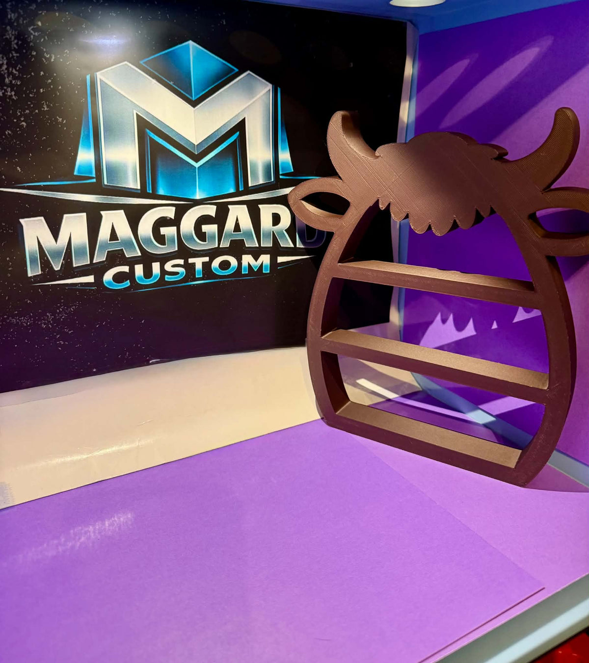 3D printed brown winged bull skull display shelf with curved horns, feathered wings, and two built-in ledges displayed in front of Maggard Custom logo