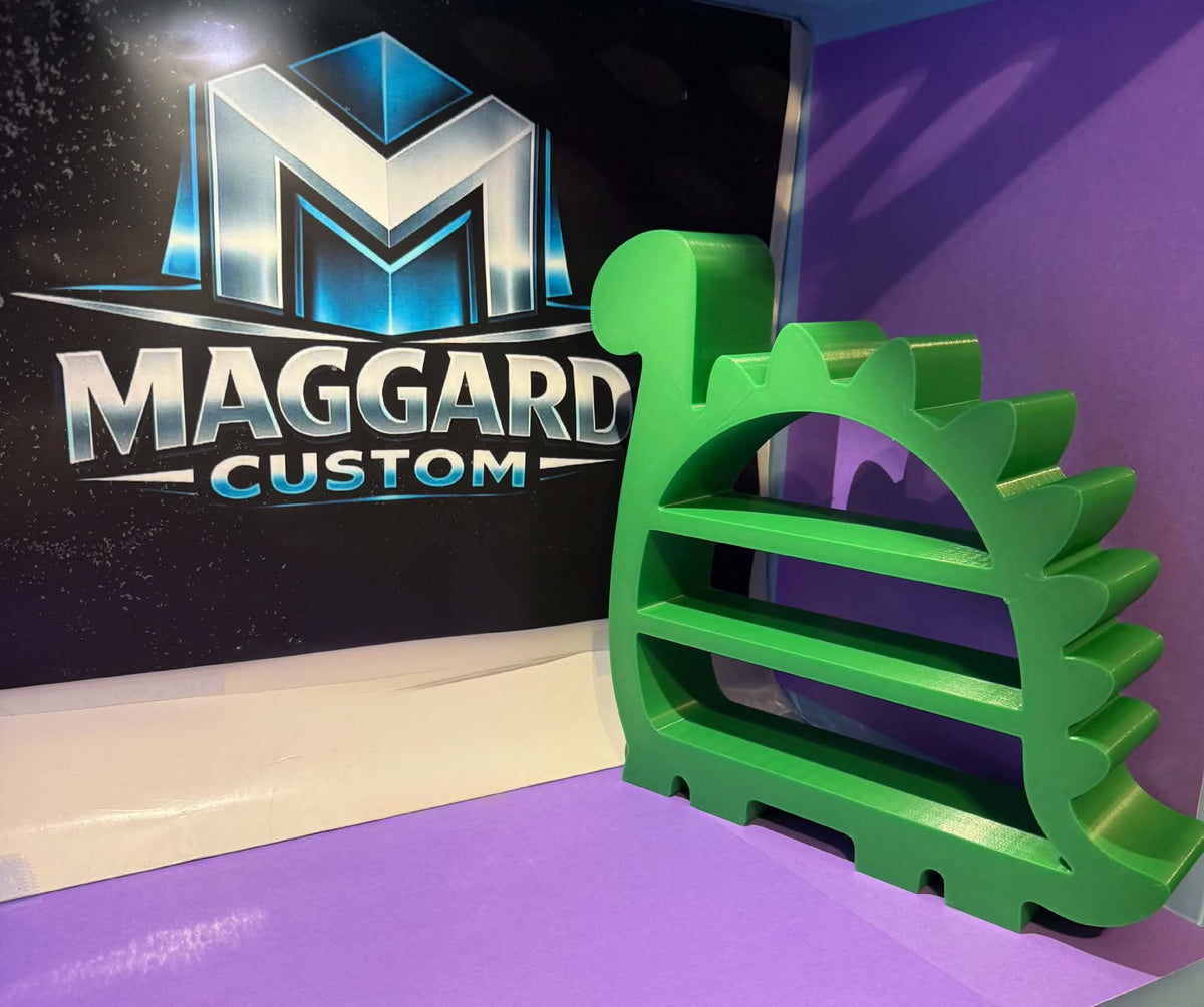 3D printed green dinosaur silhouette display shelf with spiky dorsal fins, long neck, and three built-in display ledges displayed in front of Maggard Custom logo