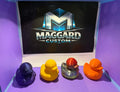 3D printed duck figurines in purple, yellow, silver metallic, and orange colors displayed in front of Maggard Custom logo
