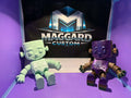 3D printed articulated monster figurines in mint green and purple with gold metallic accents displayed in front of Maggard Custom logo