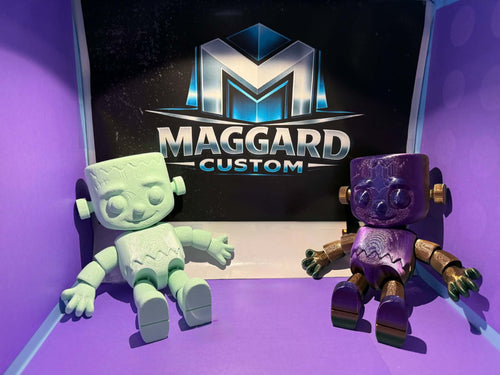 3D printed articulated monster figurines in mint green and purple with gold metallic accents displayed in front of Maggard Custom logo