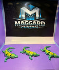 3D printed armored alligator figurines in green and yellow two-tone finish with detailed scale plates displayed in front of Maggard Custom logo