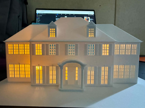 3D printed white colonial mansion replica with warm LED lighting glowing through windows