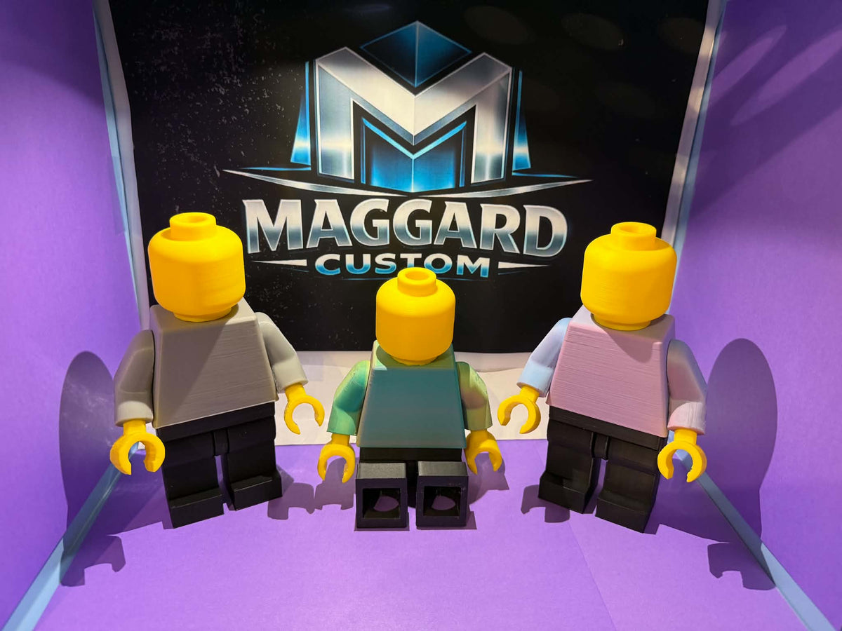 3D printed brick toy figures in gray, teal, and pink two-tone color combinations displayed in front of Maggard Custom logo