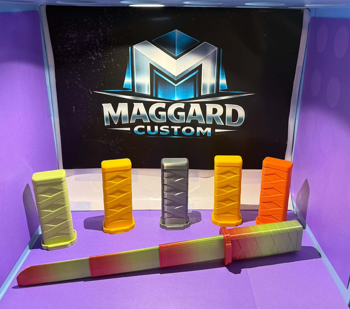 3D printed mini katana and collapsible swords in multiple colors including yellow, orange, gray, and gradient finishes displayed in front of Maggard Custom logo