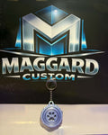 3D printed lavender blue paw print swirl keychain with raised paw center and gear-style textured border with metal keyring displayed in front of Maggard Custom logo