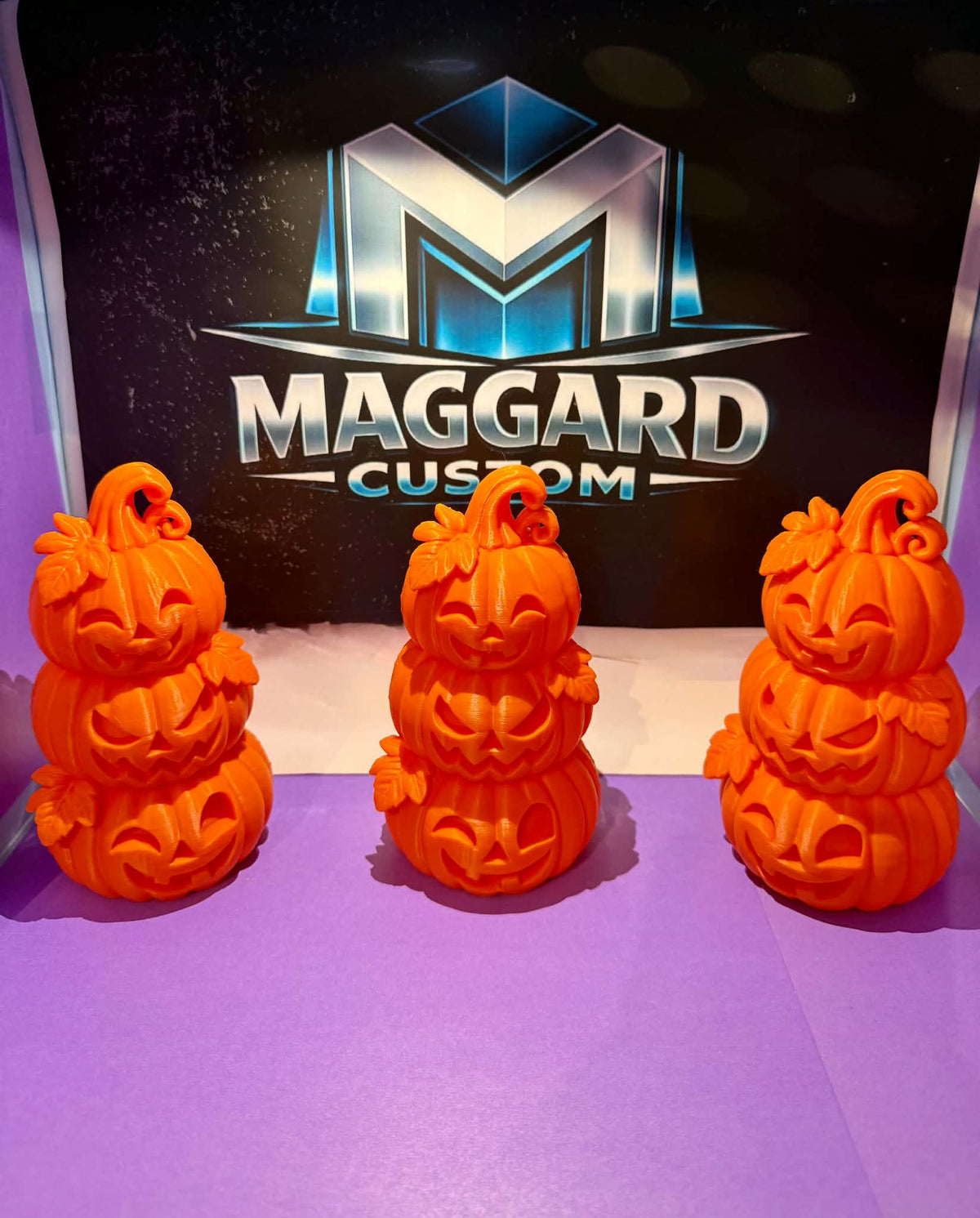 3D printed orange stacked jack-o'-lantern tower figurines with three carved pumpkins, leaf details, and curling vine stems displayed in front of Maggard Custom logo