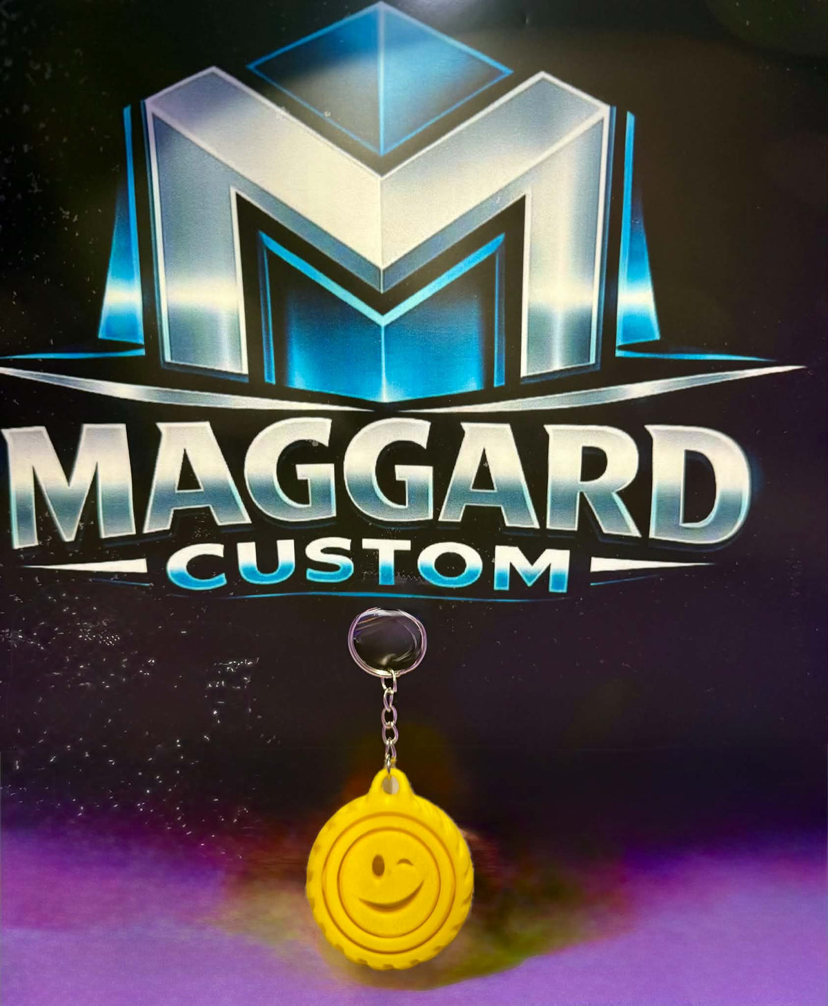 3D printed yellow smiley face swirl fidget keychain with winking face and metal keyring displayed in front of Maggard Custom logo
