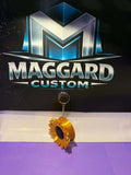 3D printed golden yellow sunflower keychain hair tie holder with layered petals and textured seed center on metal keyring displayed in front of Maggard Custom logo