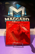 3D printed red caped hero breaking through wall bas-relief plaque with crumbling stone detail displayed on easel in front of Maggard Custom logo